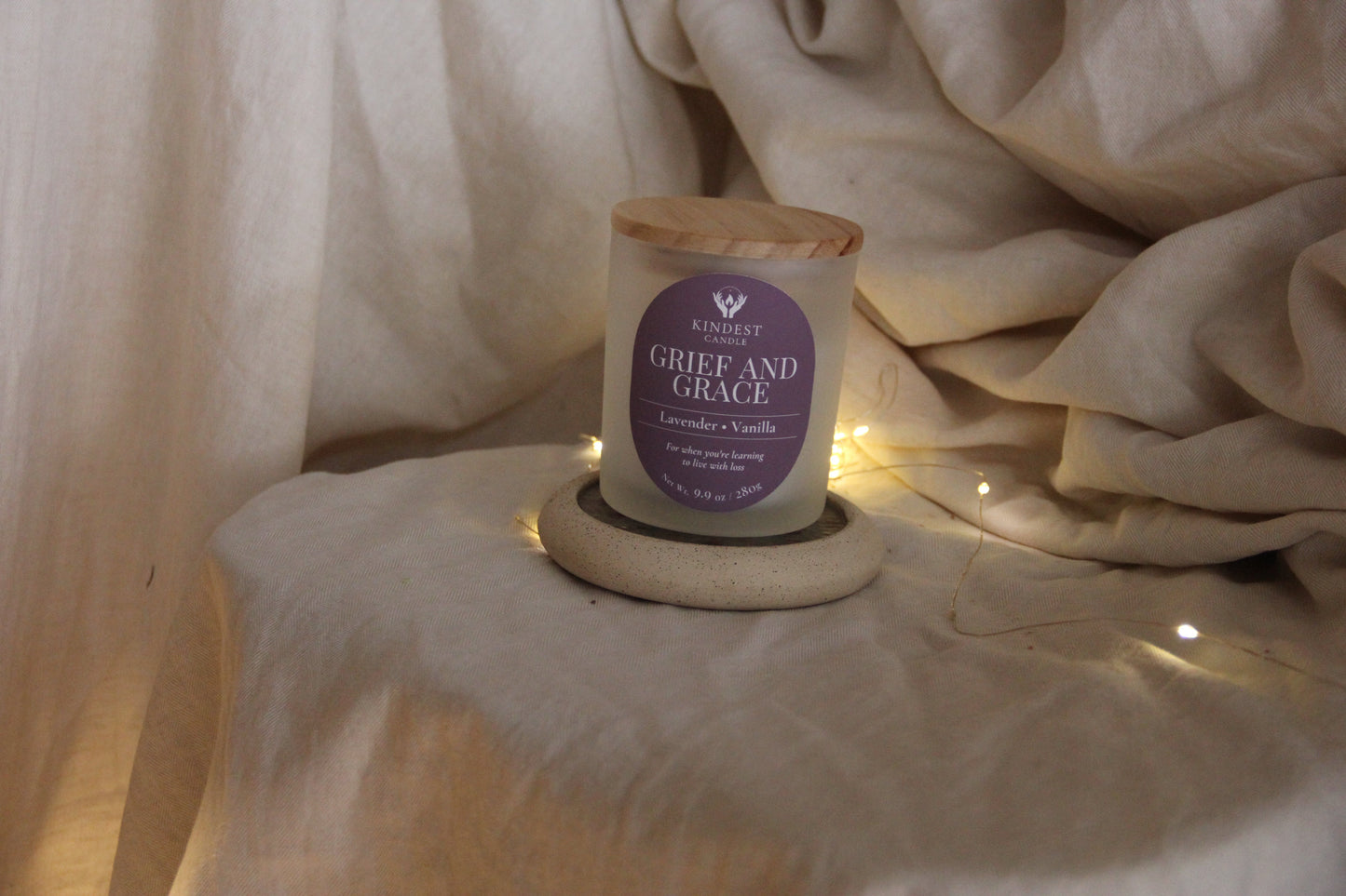 Candle labeled 'Grief and Grace' on a stone coaster with soft fabric background