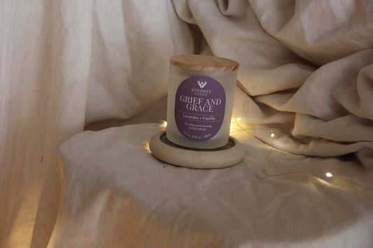 Candle labeled 'Grief and Grace' on a stone coaster with soft fabric background